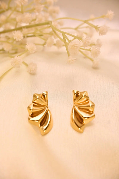 Gold-toned fan-shaped stud earrings on a soft cream background with delicate white flowers