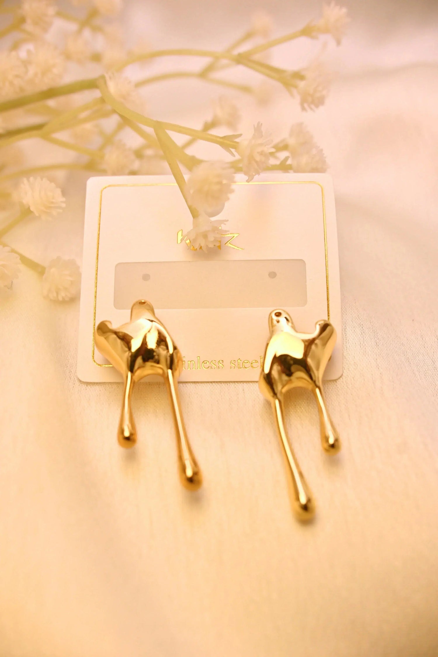 Gold abstract drop earrings on a white card with delicate floral accents, stainless steel