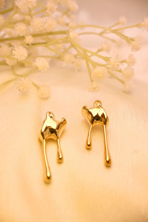 Gold abstract drop earrings on soft cream fabric with delicate white floral accents