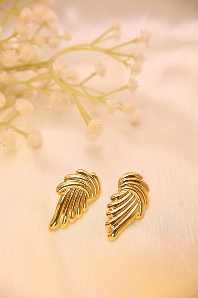 Elegant gold-plated wing-shaped stud earrings on a light fabric with delicate flowers
