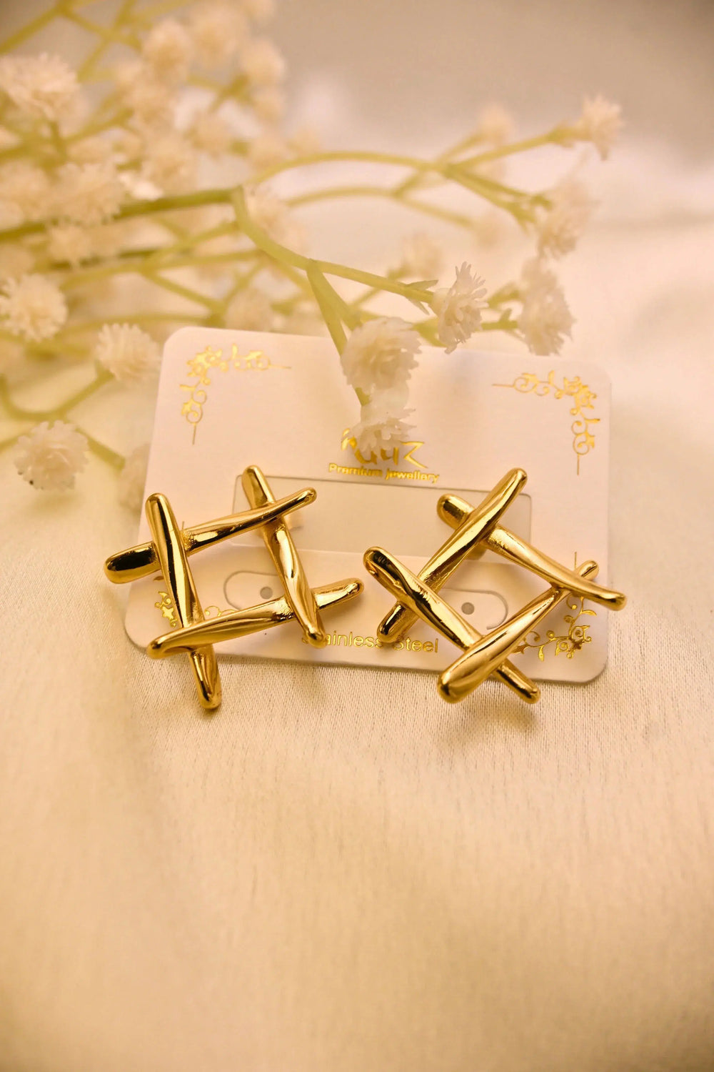 Gold geometric stud earrings on display card with white floral accents, stainless steel finish