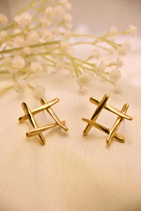 Pair of modern gold stud earrings with crisscross design on cream fabric, floral decor