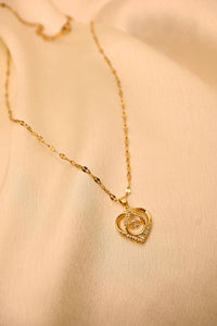 Gold heart pendant necklace with sparkling stones on a delicate chain, displayed on cream fabric