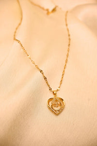 Gold chain necklace with a heart-shaped pendant featuring sparkling stones, displayed on a beige fabric.