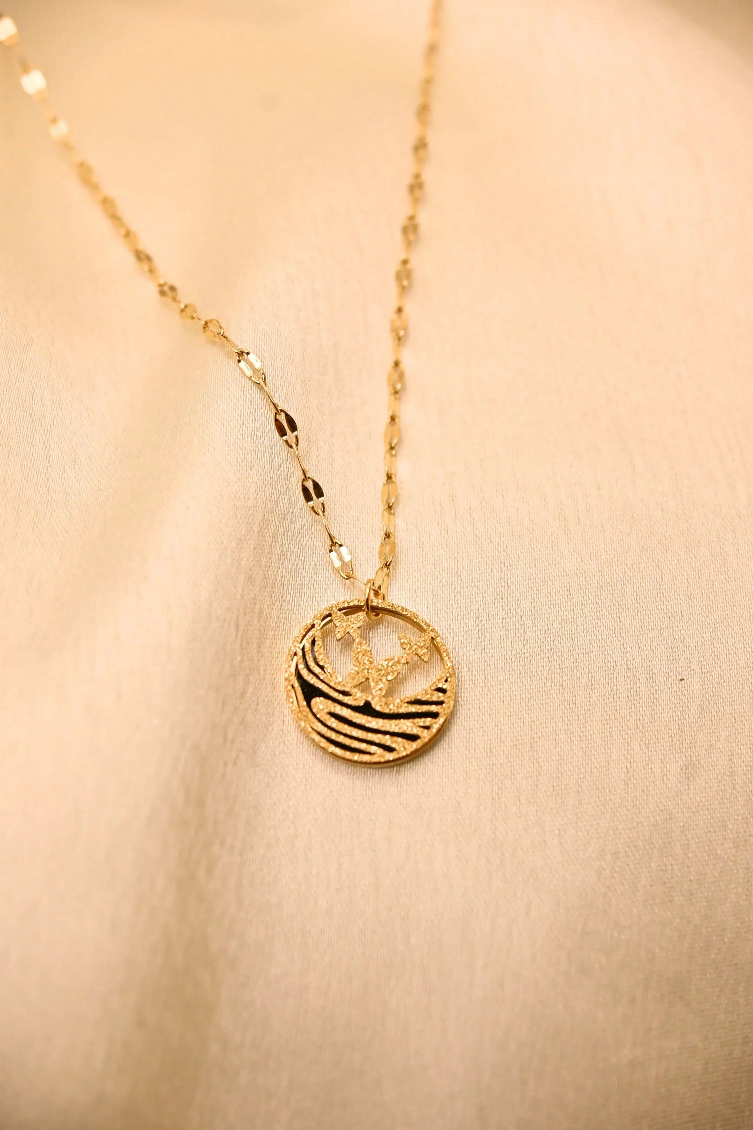 Gold pendant necklace with palm tree and wave design on textured chain, displayed on beige fabric