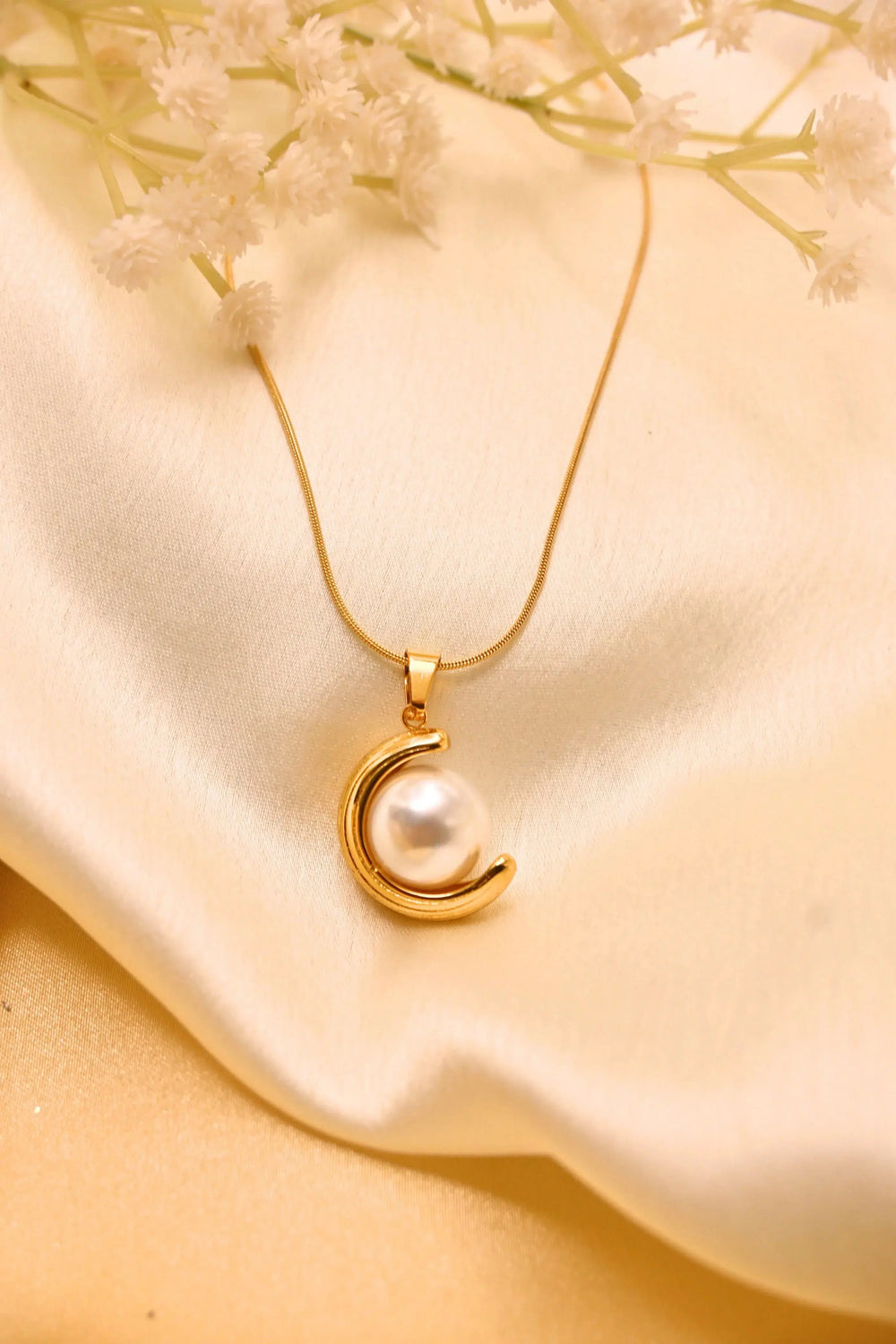 Gold chain necklace with crescent moon and pearl pendant on cream satin background