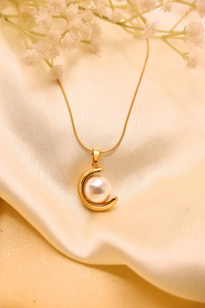 Gold chain necklace with crescent moon and pearl pendant on cream satin background