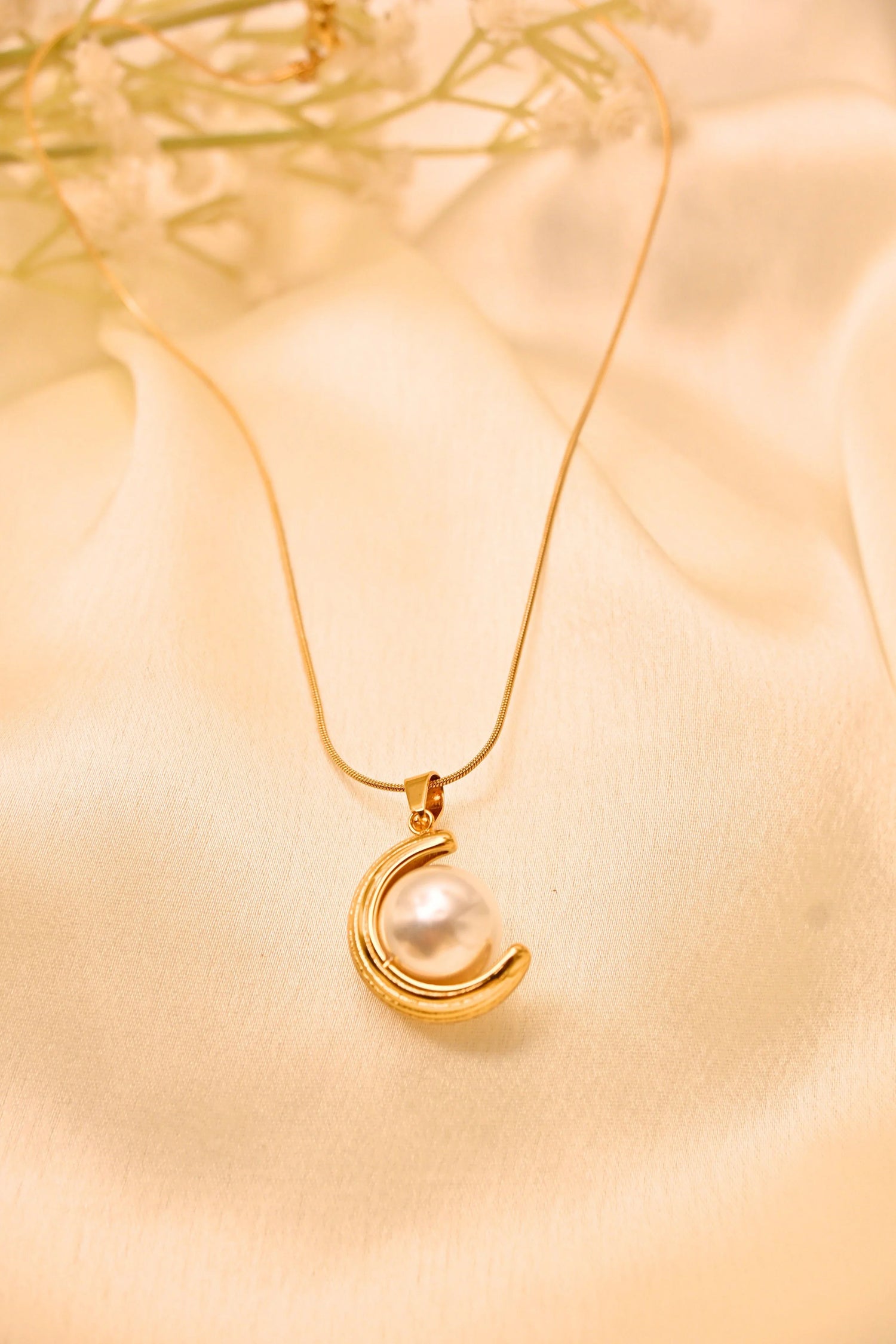 Gold necklace with crescent moon pendant and white pearl on satin fabric background