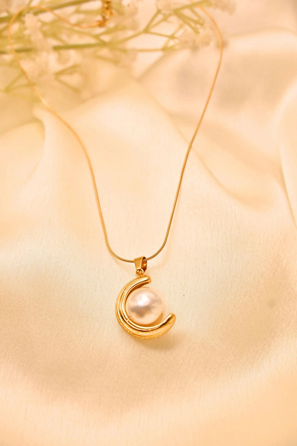 Gold necklace with crescent moon pendant and white pearl on satin fabric background