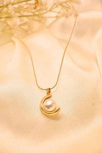 Gold necklace with crescent moon pendant and white pearl on satin fabric background