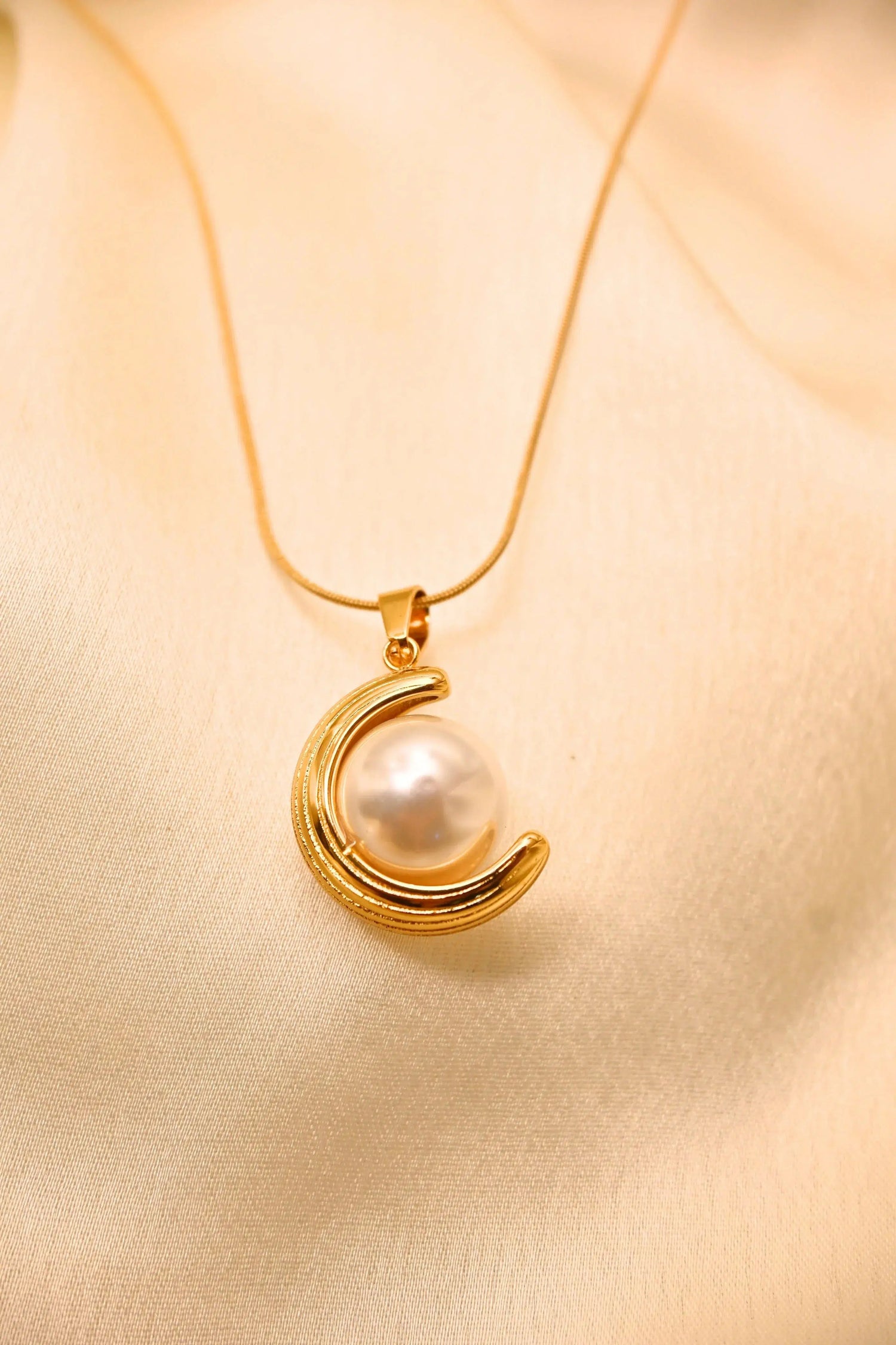 Gold crescent moon necklace with large pearl pendant on beige fabric background