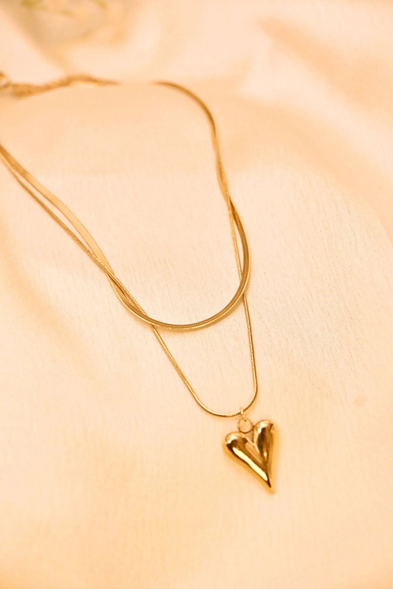 Gold layered necklace with a heart-shaped pendant on a soft beige background
