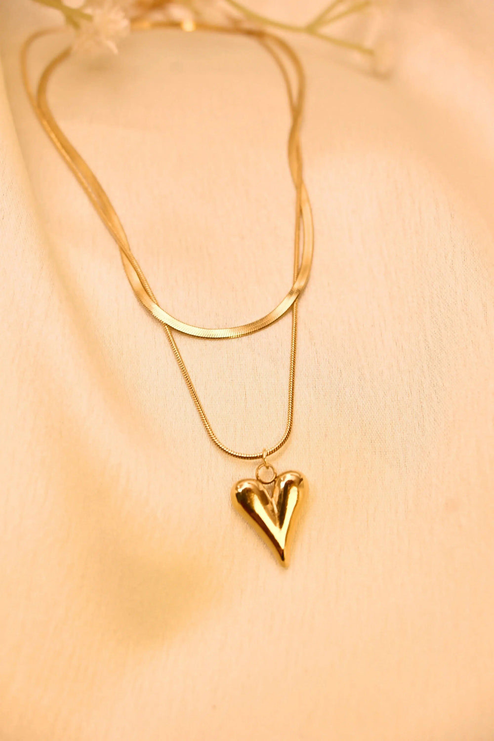 Gold heart pendant necklace with double chain on beige fabric background