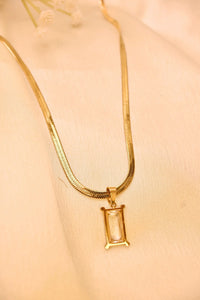 Gold necklace with a rectangular crystal pendant displayed on a beige fabric background