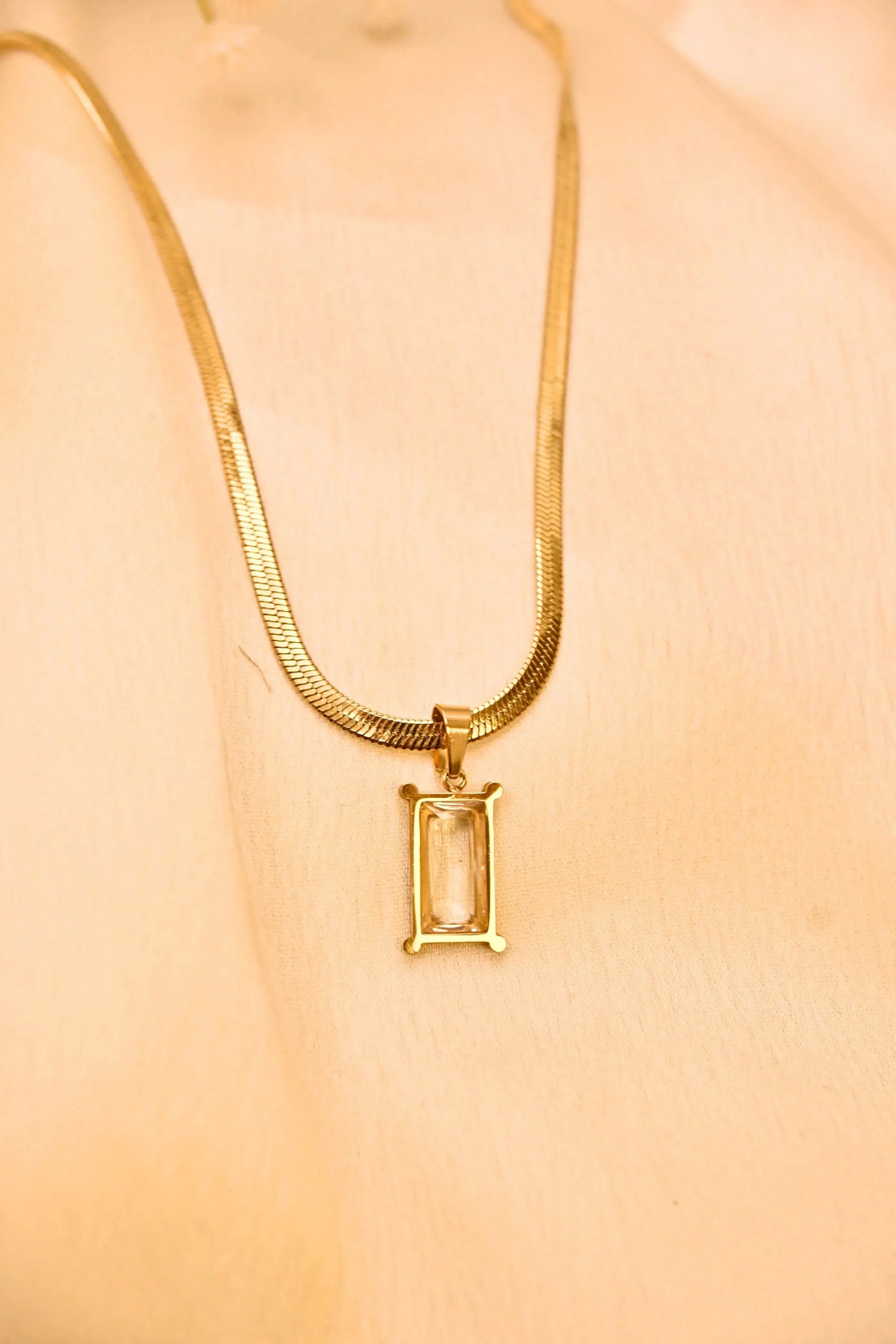 Gold chain necklace with rectangular clear stone pendant on beige background
