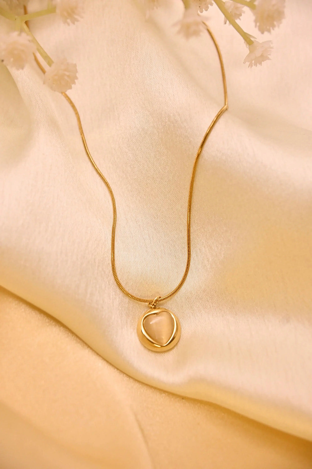 Delicate gold pendant necklace with minimalist design on a cream satin fabric