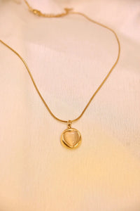Gold chain necklace with round gemstone pendant on cream fabric background