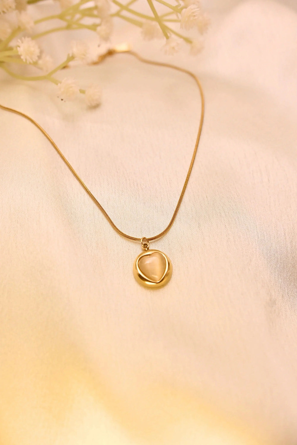 Gold chain necklace with round pendant featuring a heart-shaped center on a soft fabric background