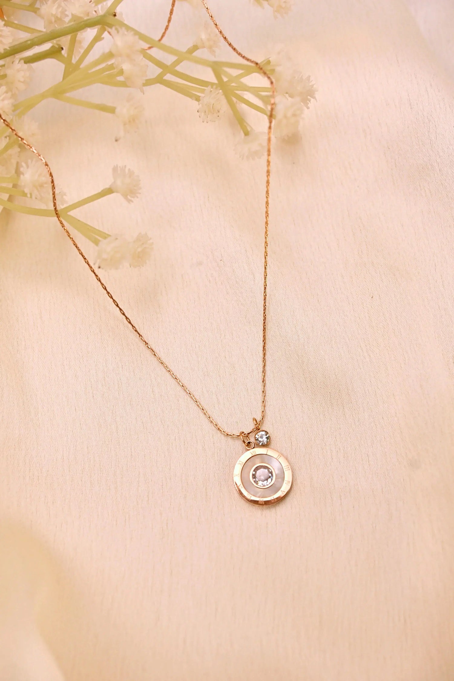 Gold pendant necklace with a round crystal charm on a soft beige fabric background