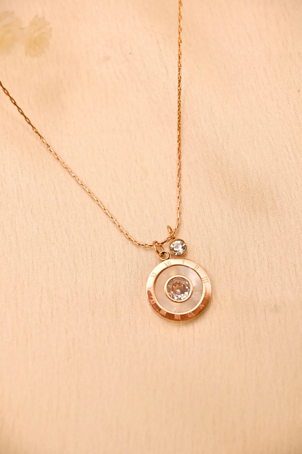 Gold chain necklace with round crystal pendant on beige background