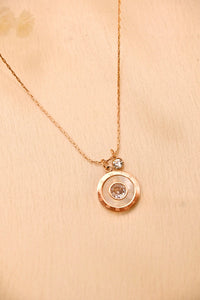Gold chain necklace with round crystal pendant on beige background