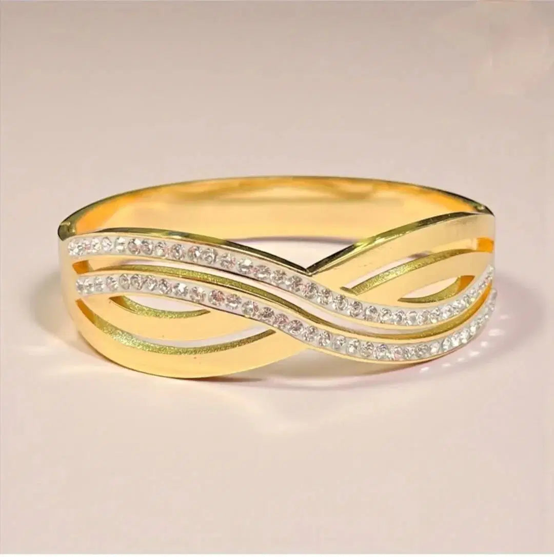 Gold bangle bracelet with crisscross design and embedded shimmering stones on a plain background