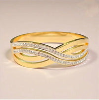 Gold bangle bracelet with crisscross design and embedded shimmering stones on a plain background