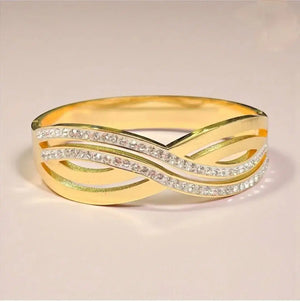 Gold bangle bracelet with crisscross design and embedded shimmering stones on a plain background