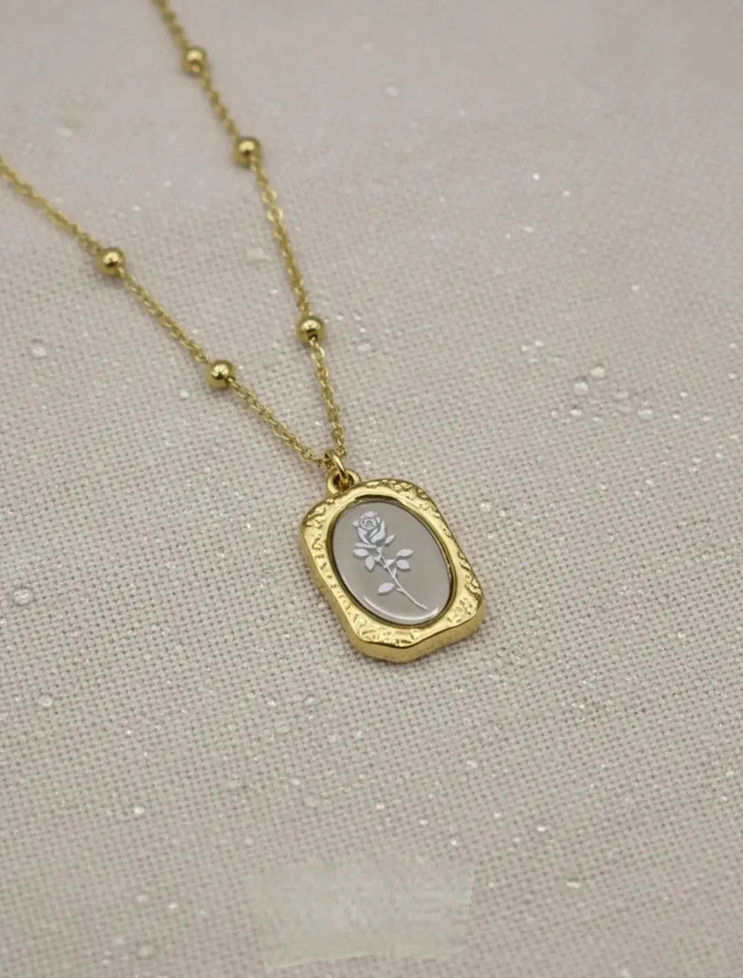 Gold chain necklace with oval rose flower pendant on textured fabric background