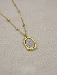 Gold chain necklace with oval rose flower pendant on textured fabric background