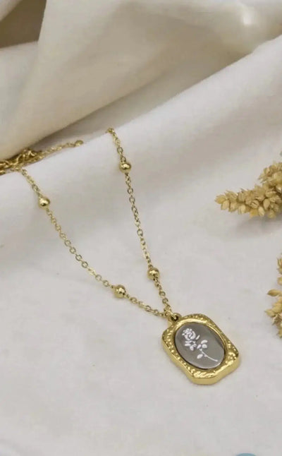 Gold necklace with floral pendant on a white fabric background, elegant jewelry design
